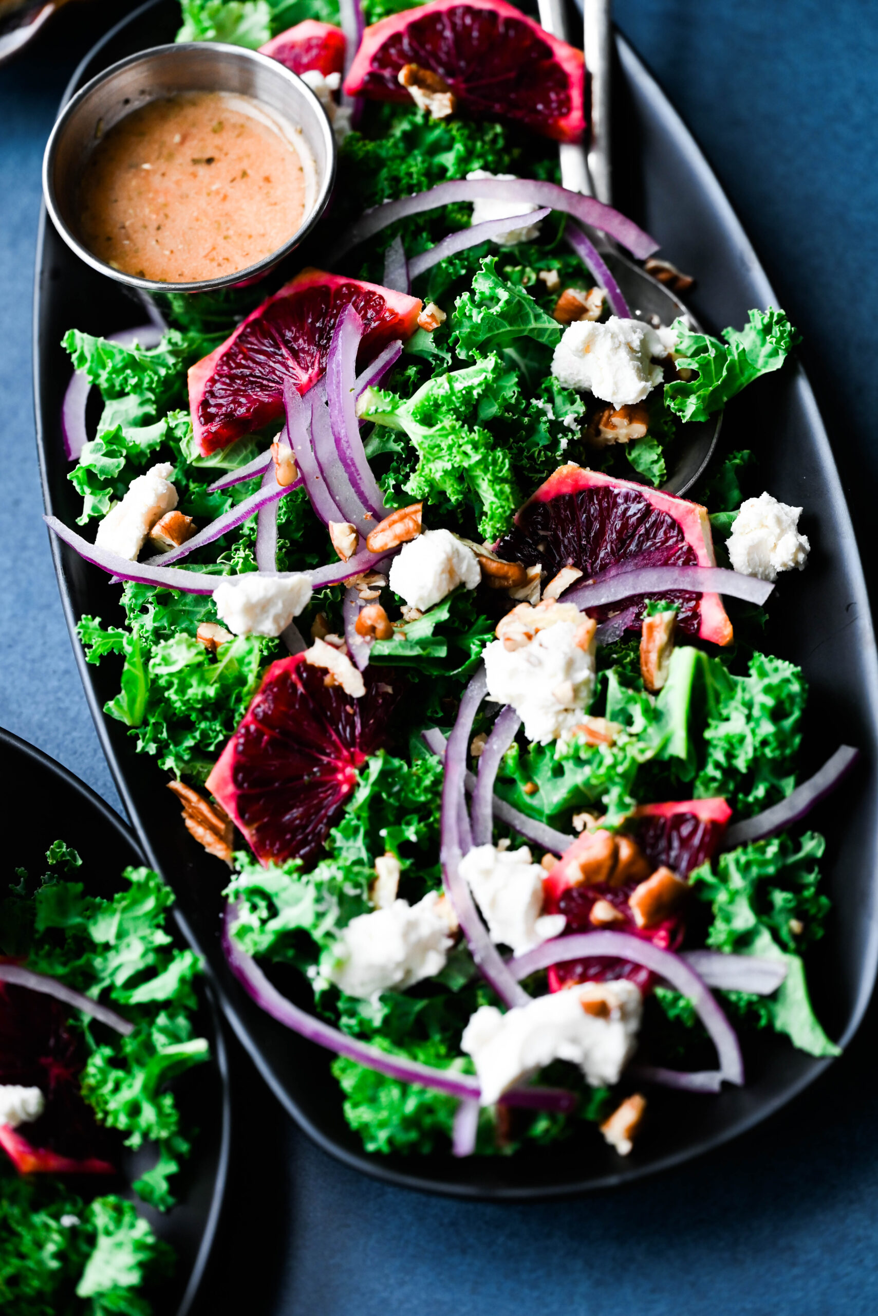 A blood orange kale salad on a black plate. 