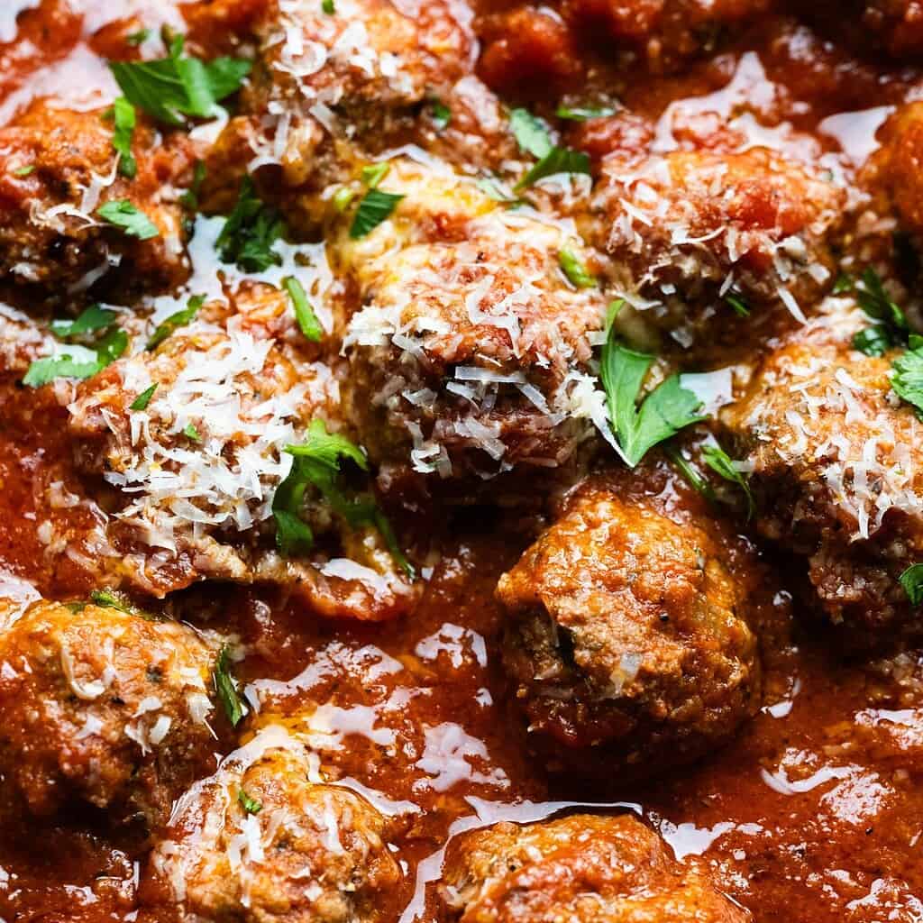Close up image of meatballs in tomato sauce with cheese and parsley.