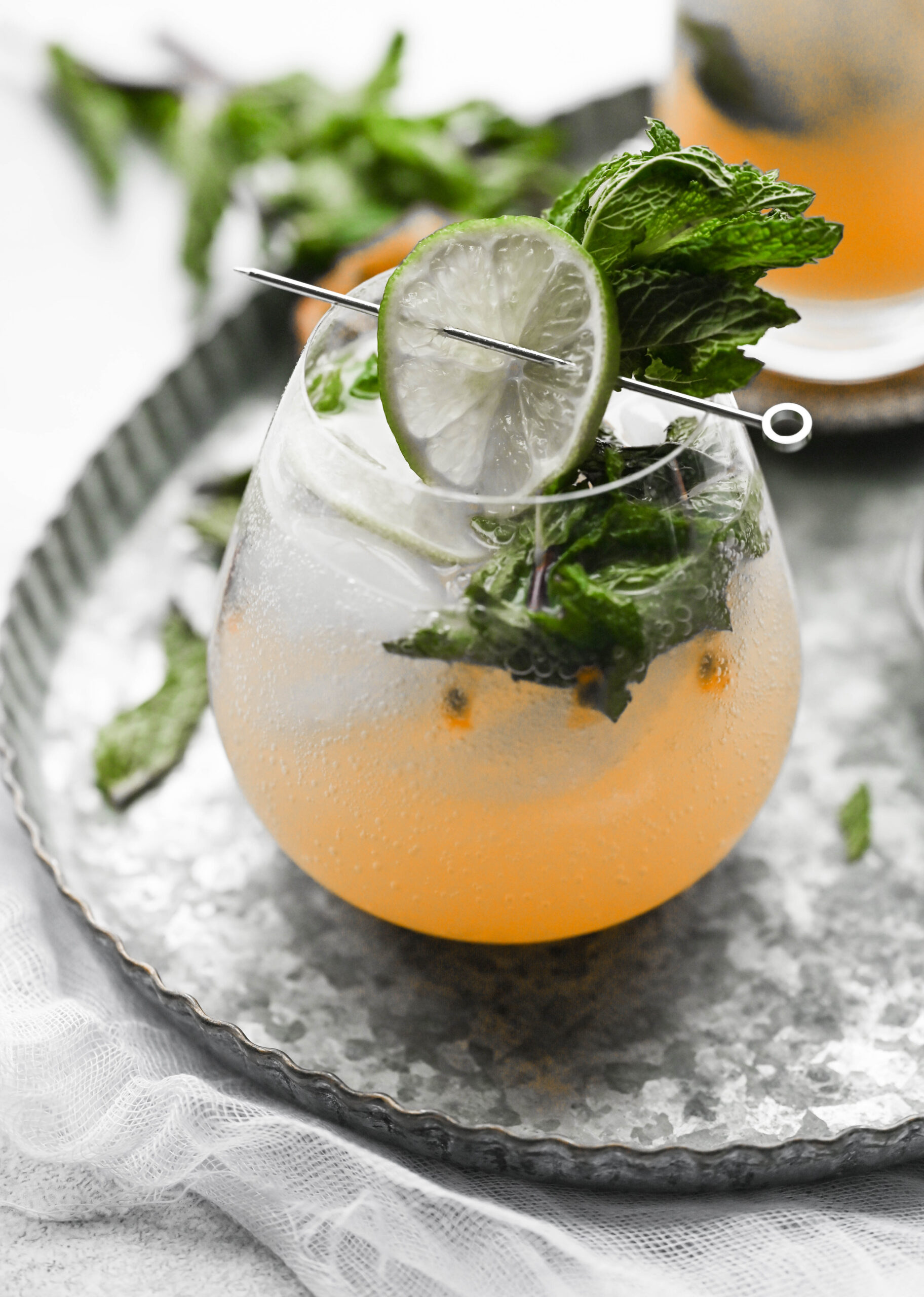 Passion Fruit Mojito Mocktail with mint leaves and a lime for garnish on a silver plate. 