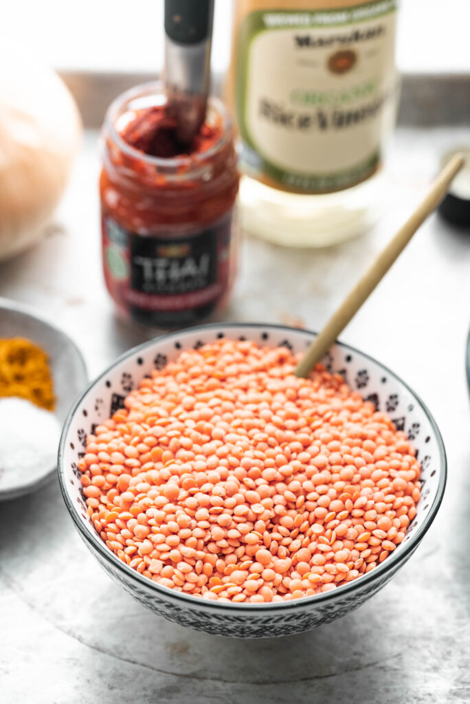 Photo of red lentils in a bowl with Thai Curry paste in the background. 