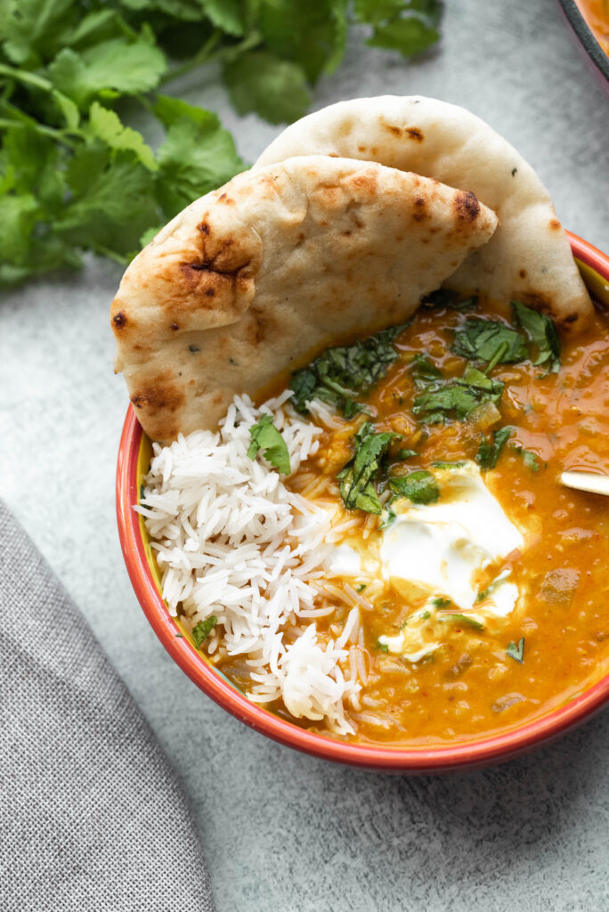 Chickpea and Lentil Curry with rice and chopped cilantro with naan bread in a red bowl. 