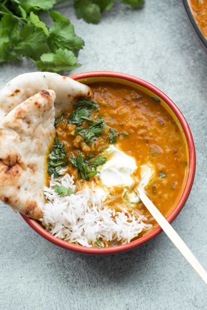 Easy Chickpea and Lentil Curry in an orange bowl with cilantro, and naan bread.  