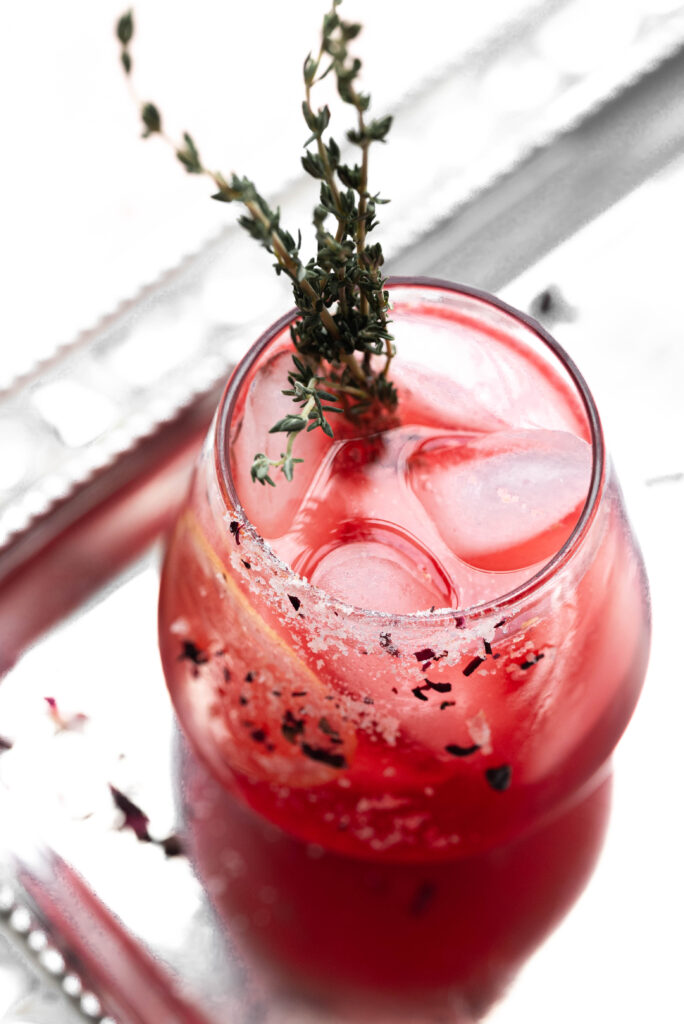 Rose mocktail in a small wine glass with ice and garnished with fresh Thyme. 