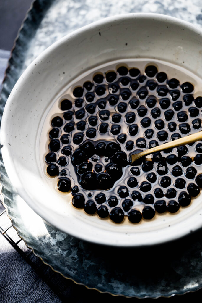 Cooked boba in a white speckled owl with a gold spoon.  