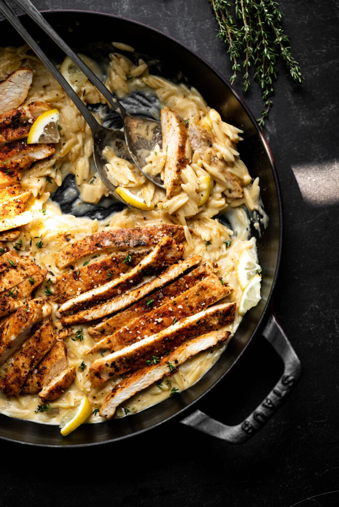 Black pan on a black background with orzo and chicken. 