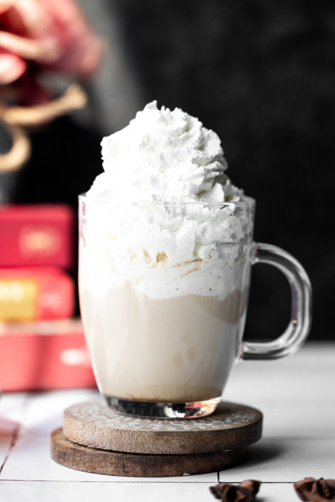 Chai tea latte in a clear cup with lots of whipped cream. 