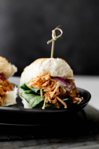 Pulled chicken on a Hawaiian bun with lettuce on a black plate.