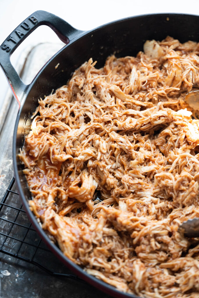 Photo of shredded chicken in a dutch oven with bbq sauce. 