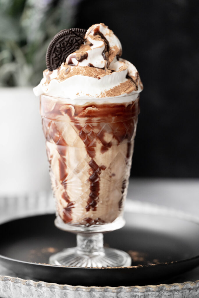 Oreo Iced Coffee in a pretty glass garnished with whipped cream. 