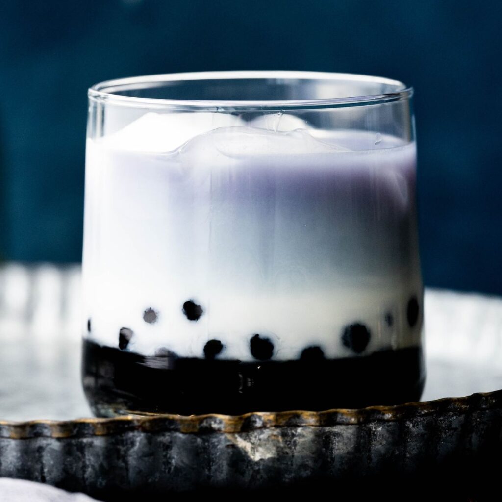 Butterfly pea bubble tea in a short glass with bubbles on the bottom, and blue-ish tea on top.  