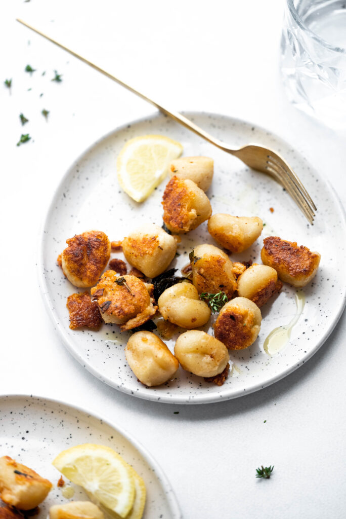 Pan fried gnocchi on a speckled plate with a lemon wedge and olive oil. 