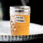 Labeled mason jar with salted caramel coffee syrup on a silver plate.