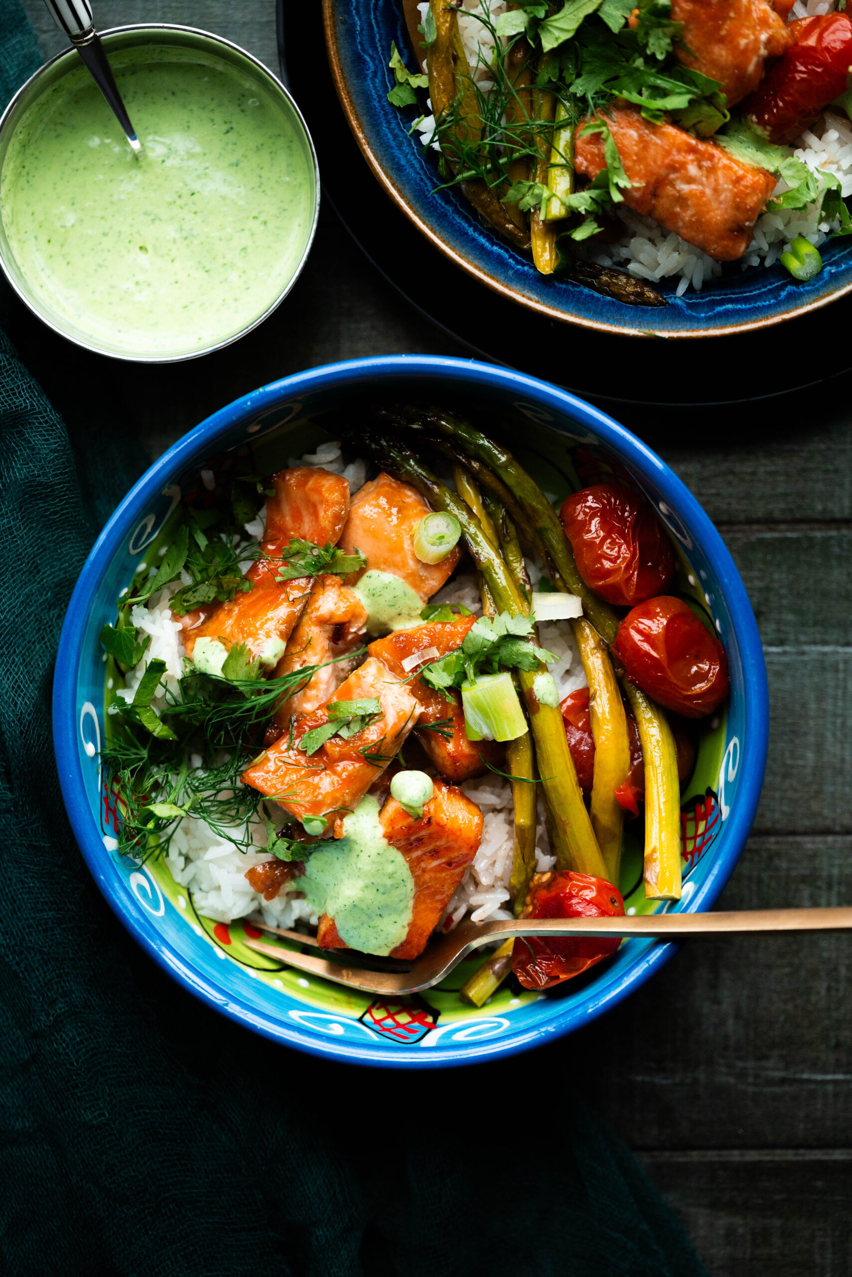 Overheat shot of salmon, asparagus, and tomatoes in a blue bowl with sauce. 
