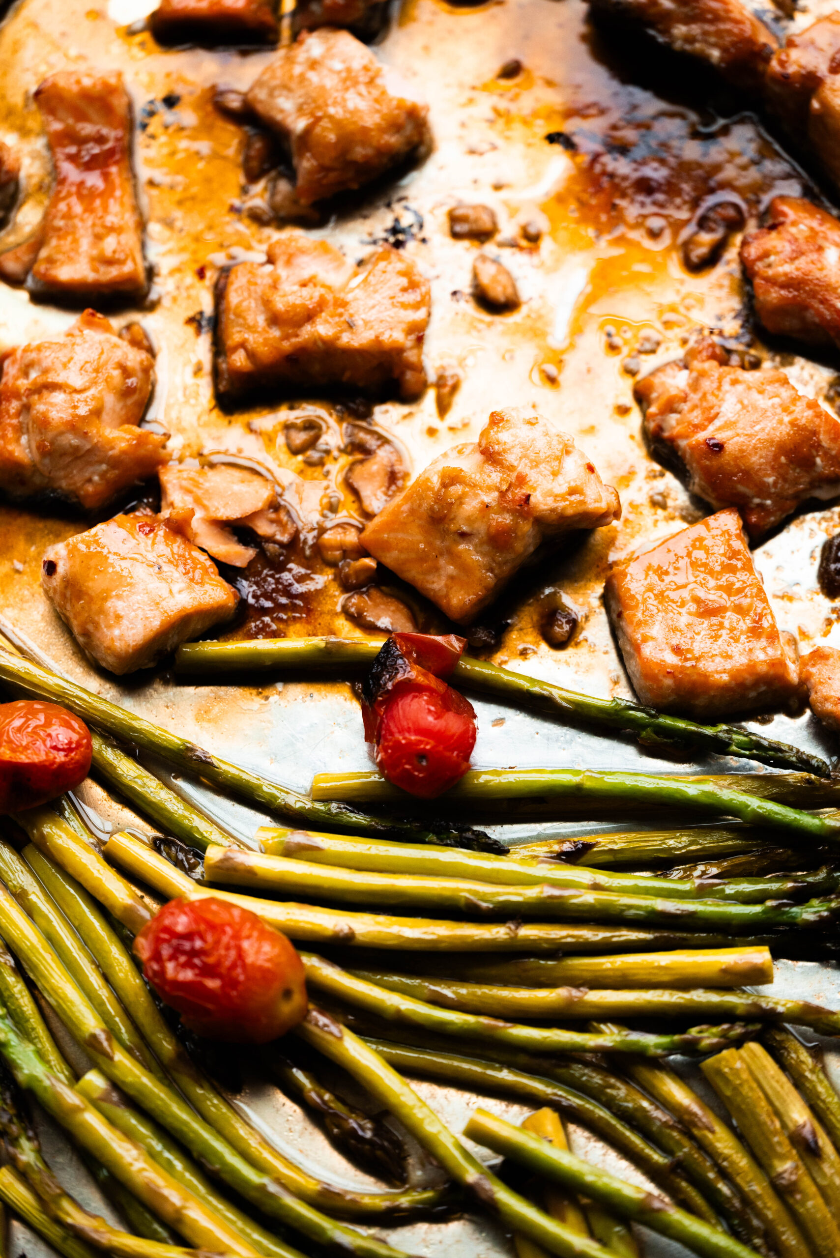 Photo of salmon bites with blistered tomatoes and asparagus on a sheet pan. 