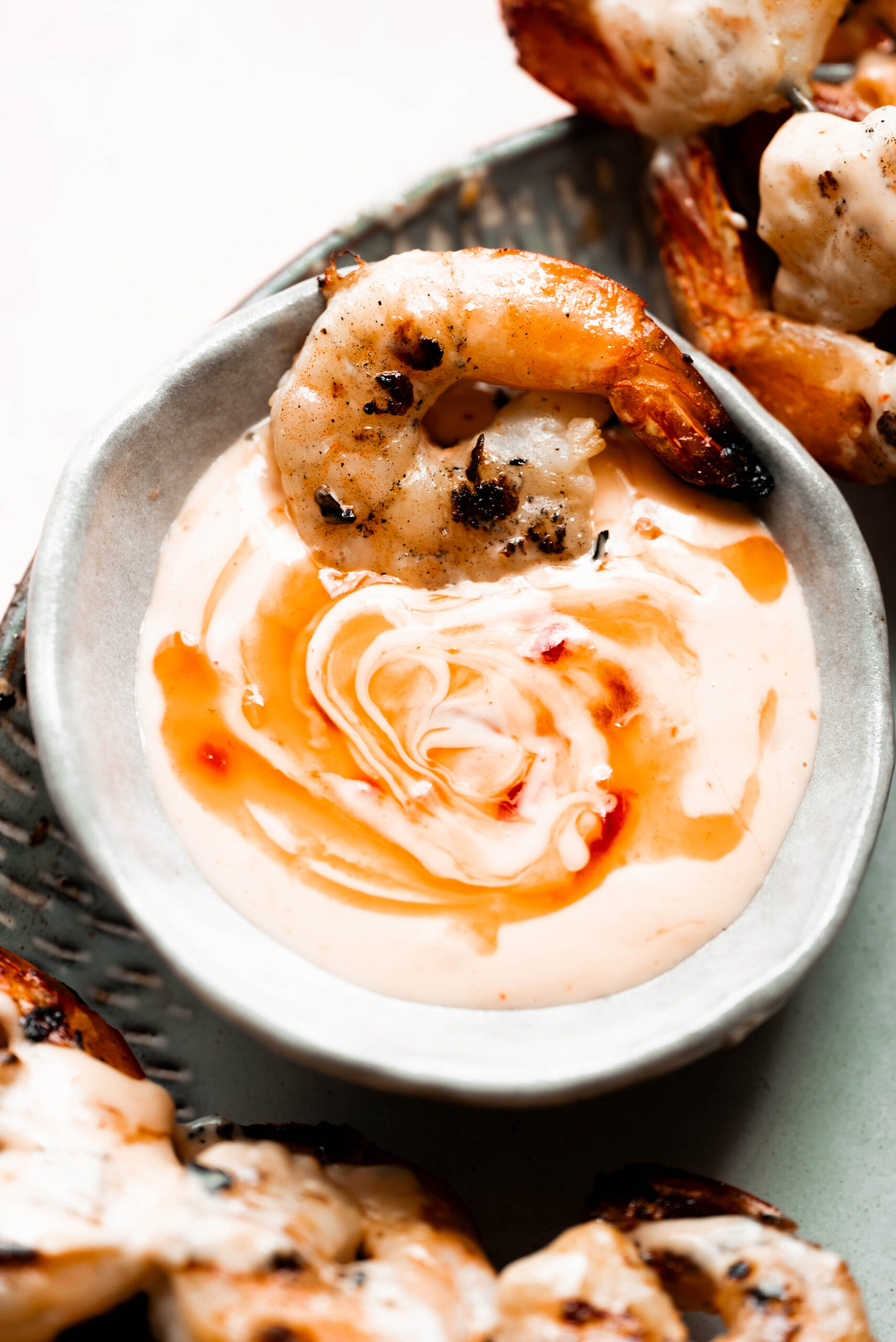 Grilled shrimp being dipped into a bowl of bang bang sauce. 