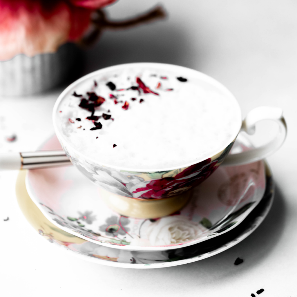 Photo of a tea cup with roses filled with a rose latte and rose petals. 