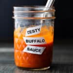 Labeled mason jar "zesty Buffalo Sauce" on a wooden board.