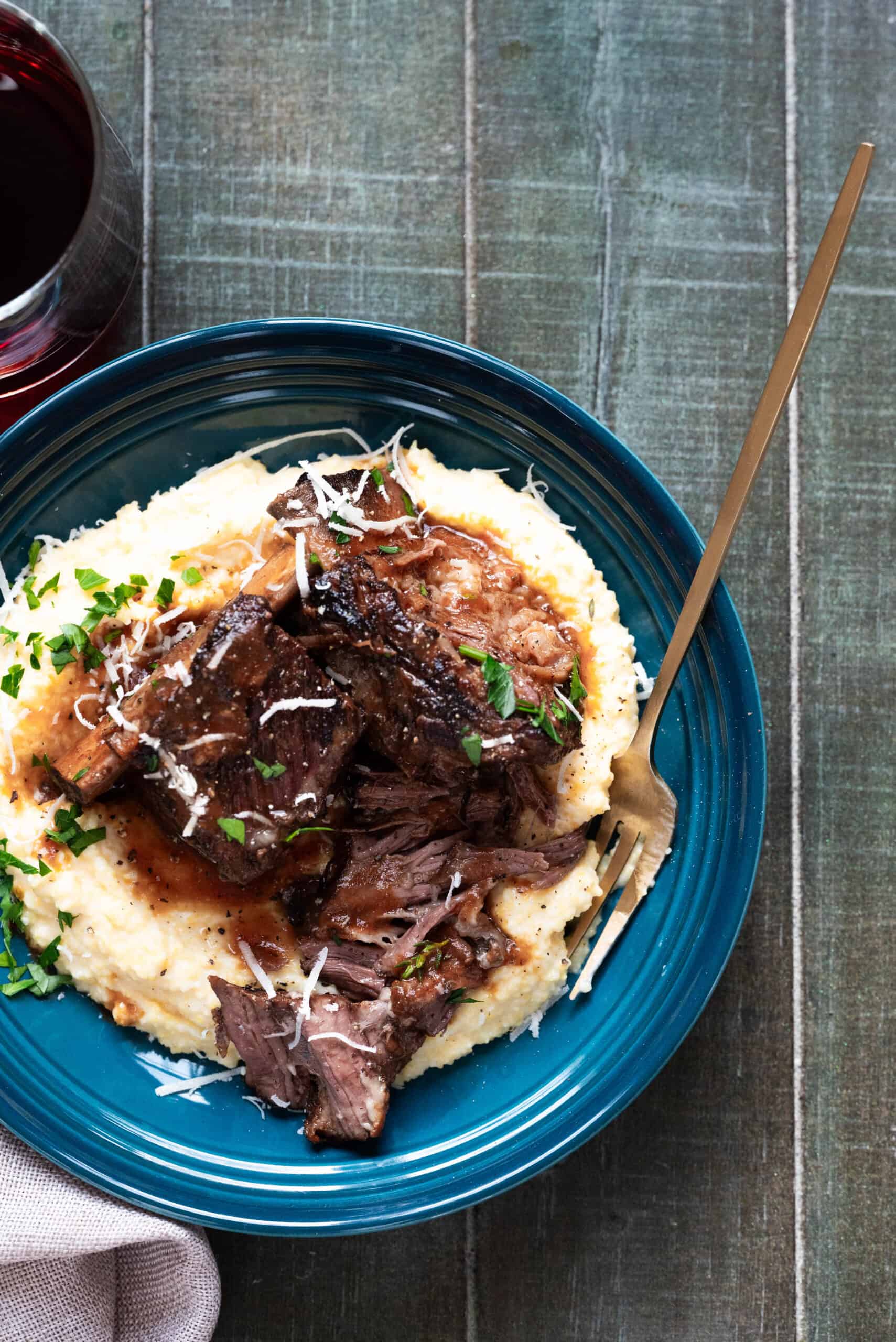 Short ribs on a wooden background in a blue bowl with a gold fork. 