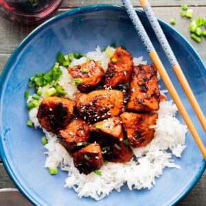 Honey garlic salmon bites over rice in a blue bowl.