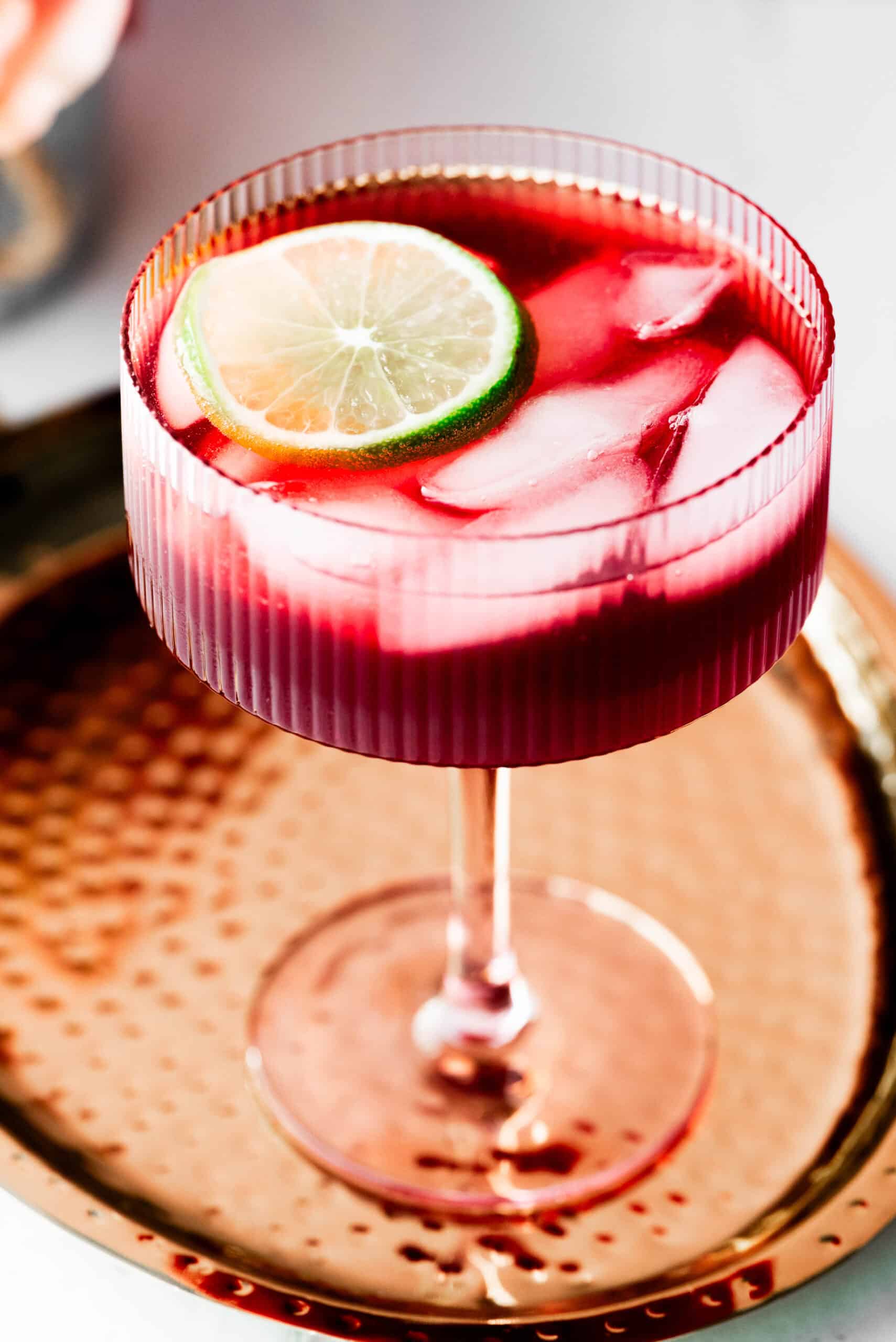 Angle shot of tart cherry mocktail in a pink glass on a gold plate. 