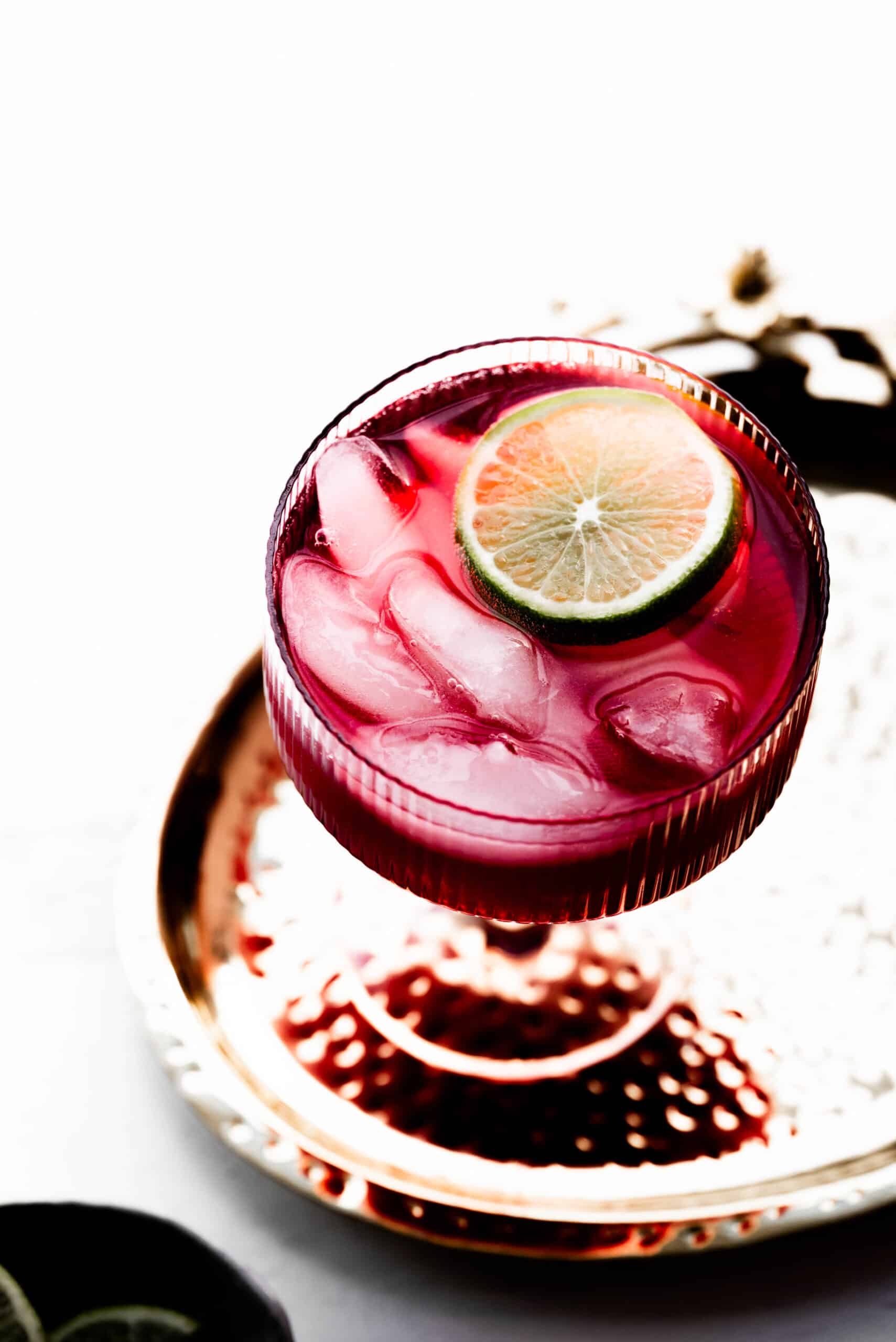 Overhead image of a tart cherry juice mocktail in a pink glass with a lime wedge. 
