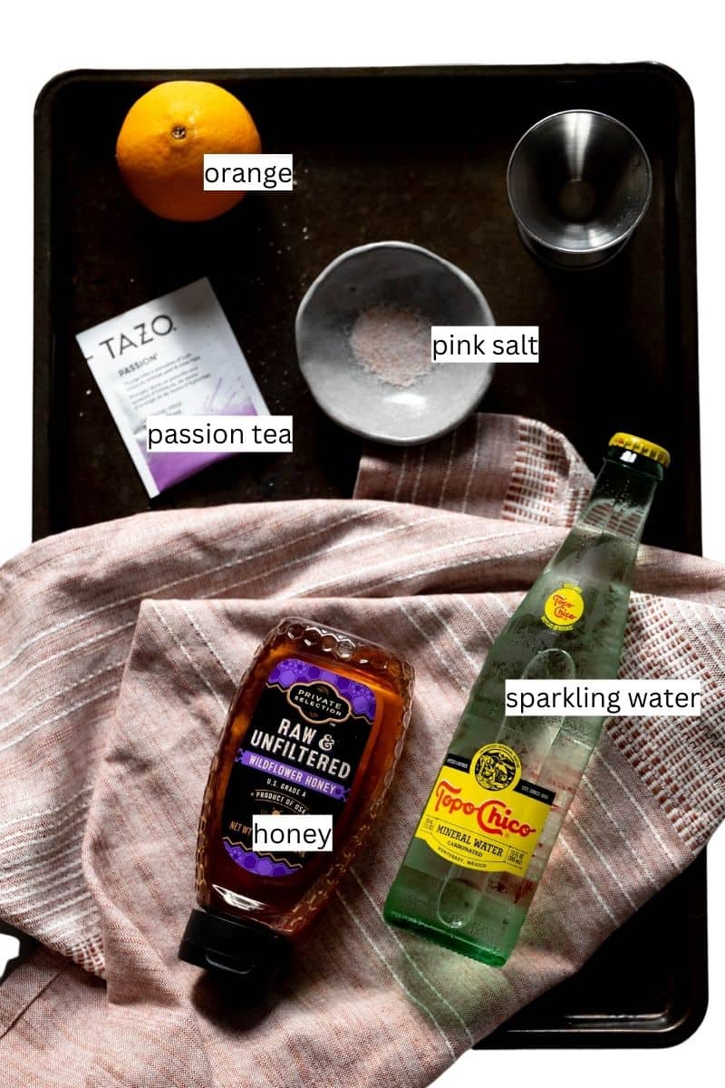 Ingredients needed to make an orange passion mocktail on a sheet pan with labels. 