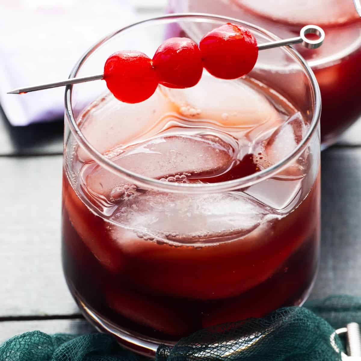 Hero image: kava mocktail with ice and cherries in a low ball glass. 