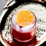 Hero image of an orange passion mocktail in a short glass on a gold plate.