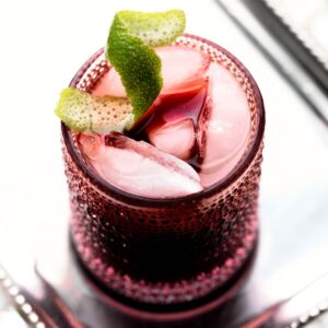 Sleepy mocktail in a pink glass with a lime twist on a plate.