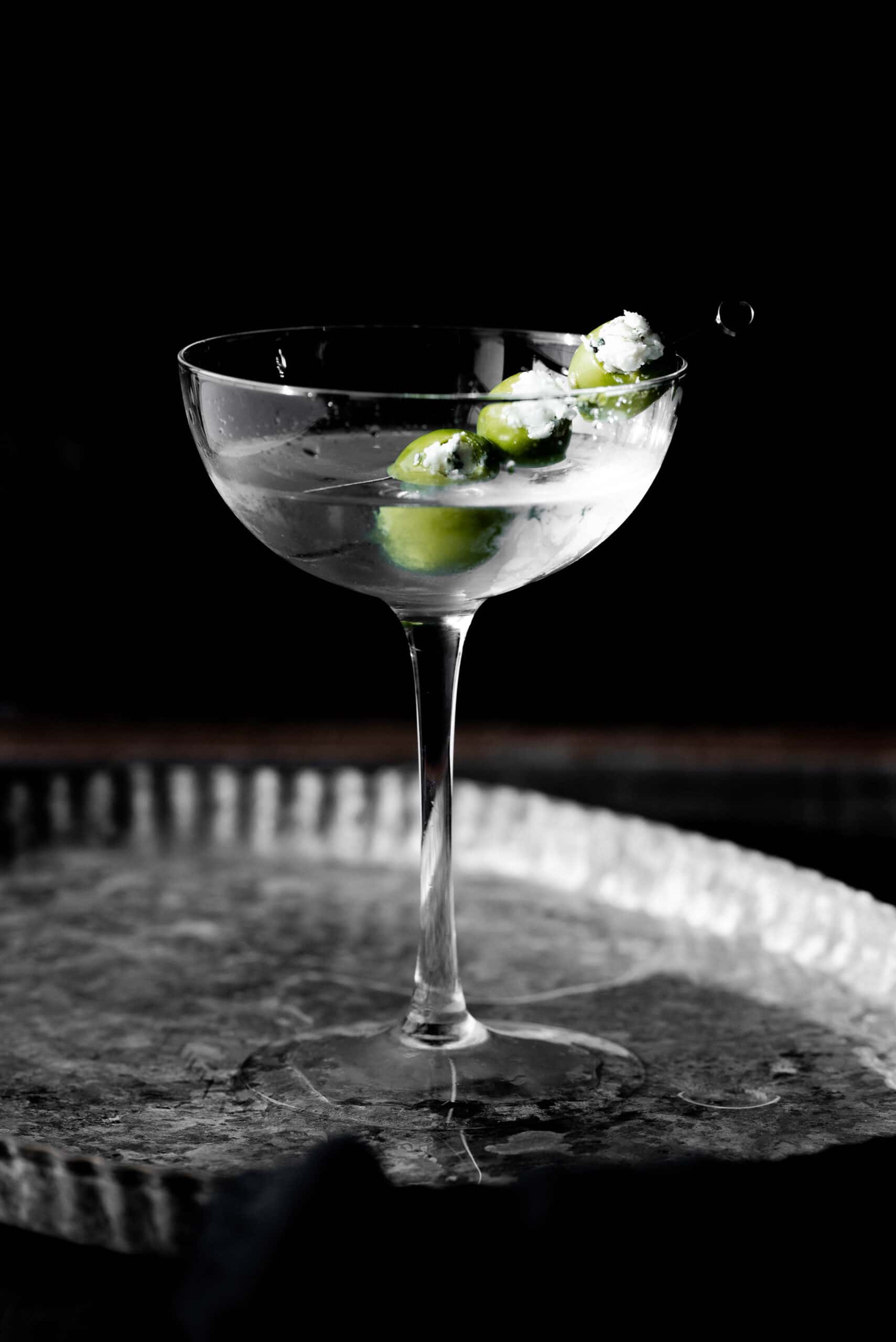Straight on shot of a martini mocktail with hand stuffed, blue cheese stuffed olives. 