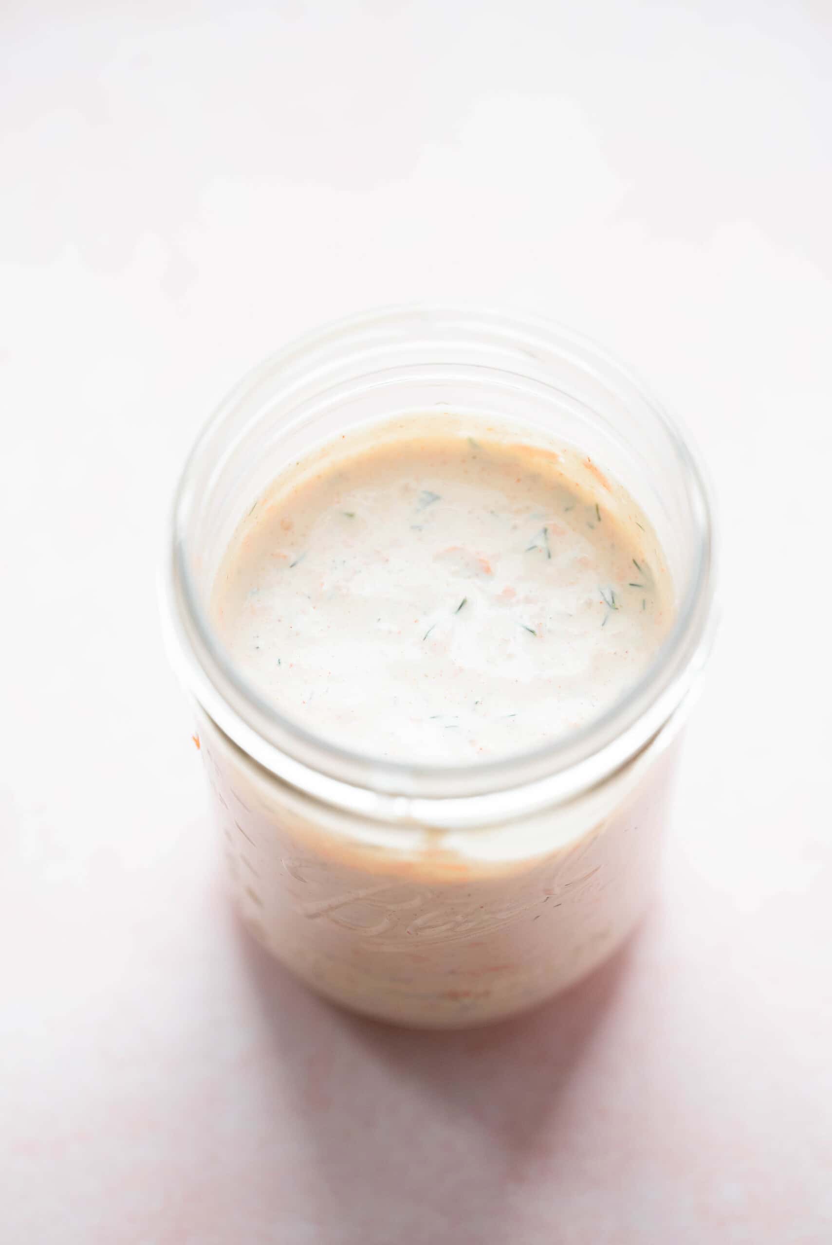 Garden Herb Ranch dressing in a mason jar on a pink background.