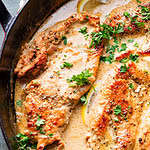 Creamy Lemon Chicken - featured in a red, shallow dutch oven with parsley garnish.