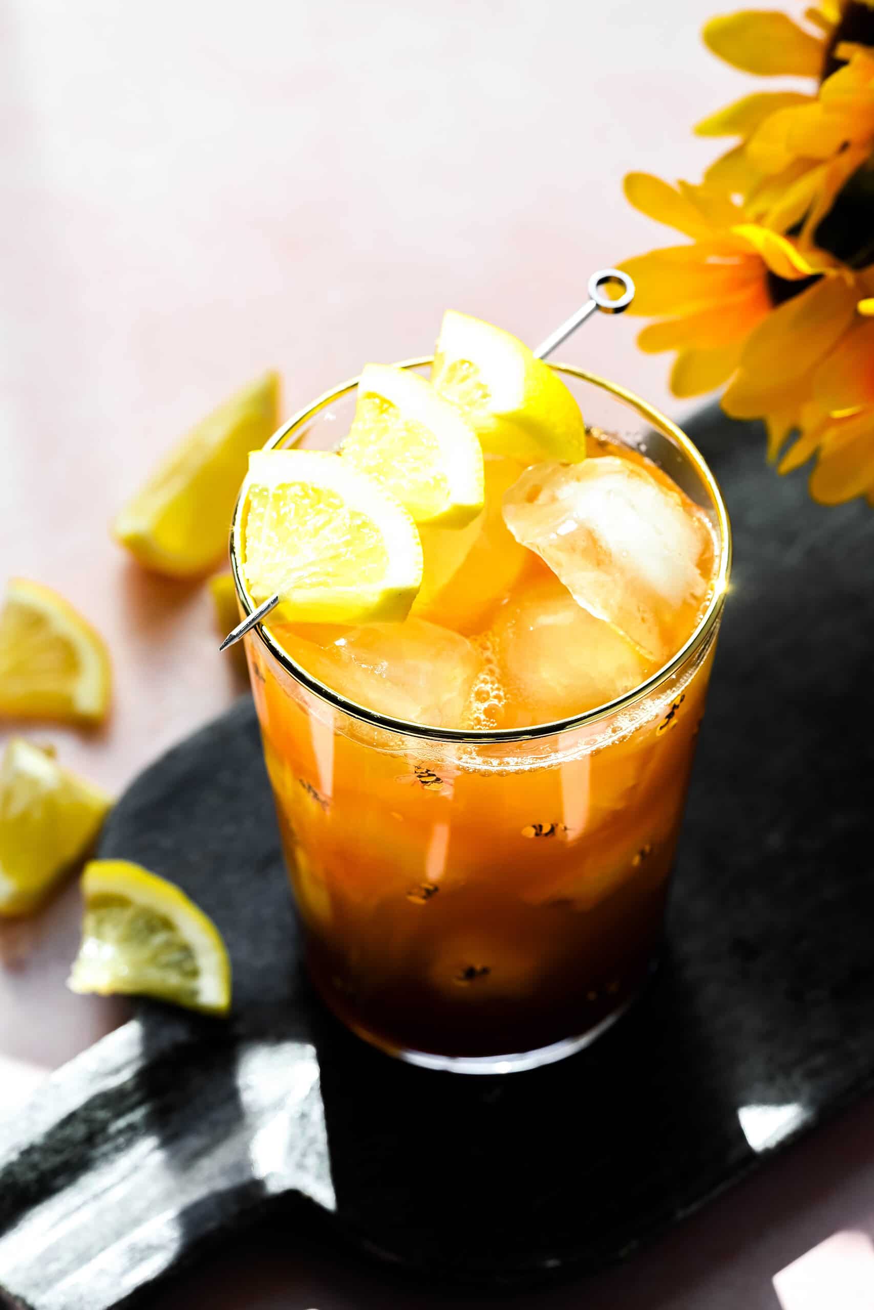 Angled overhead image of tea in a glass with ice on a black board. 