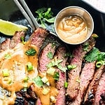 Hero image of flank steak with toppings on a black pan.