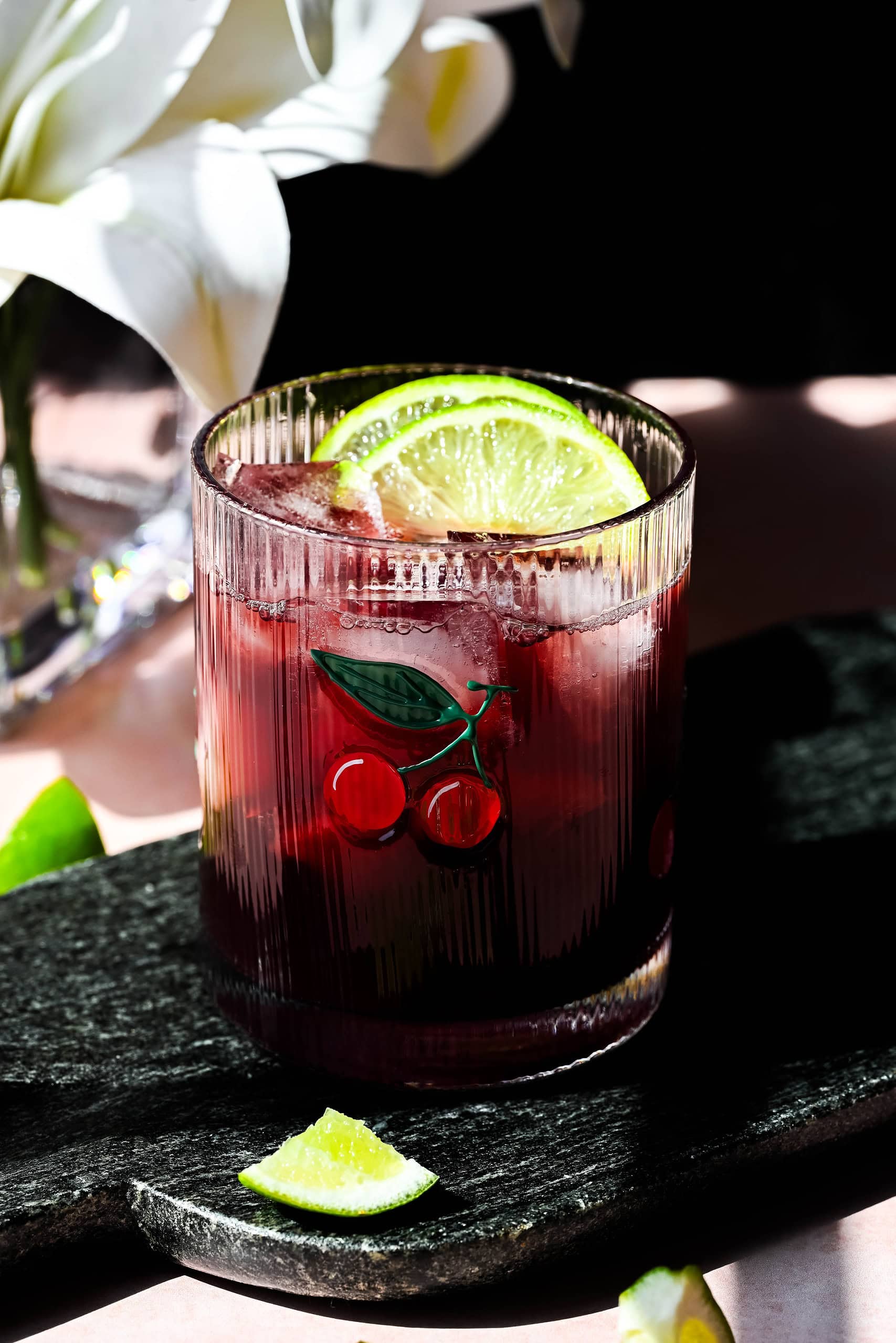 Image of a cherry mocktail with a cute glass on a black stone board. 