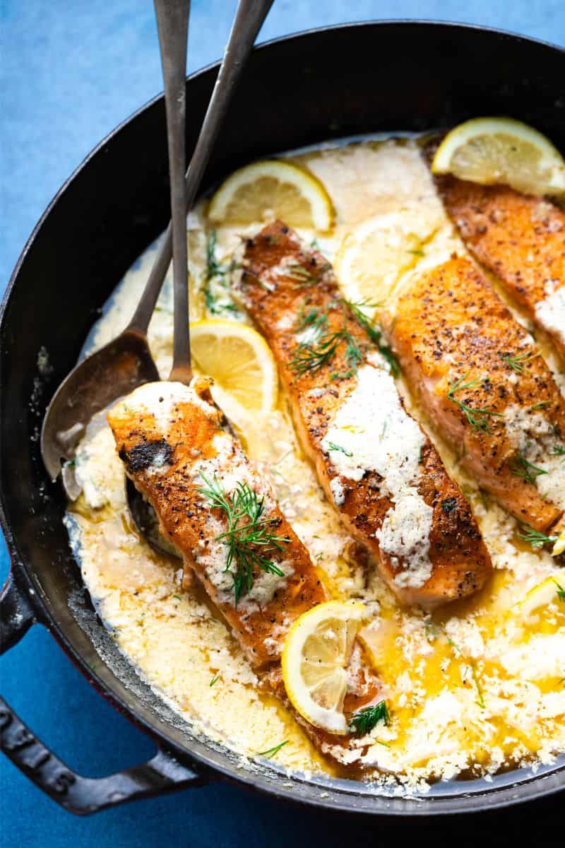 Salmon in a pan with cream sauce and lemon dill garnish. 