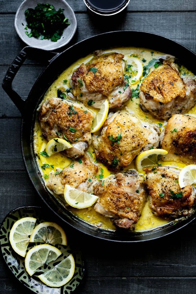 Chicken Thighs on a table with lemon wedges and parsley. 