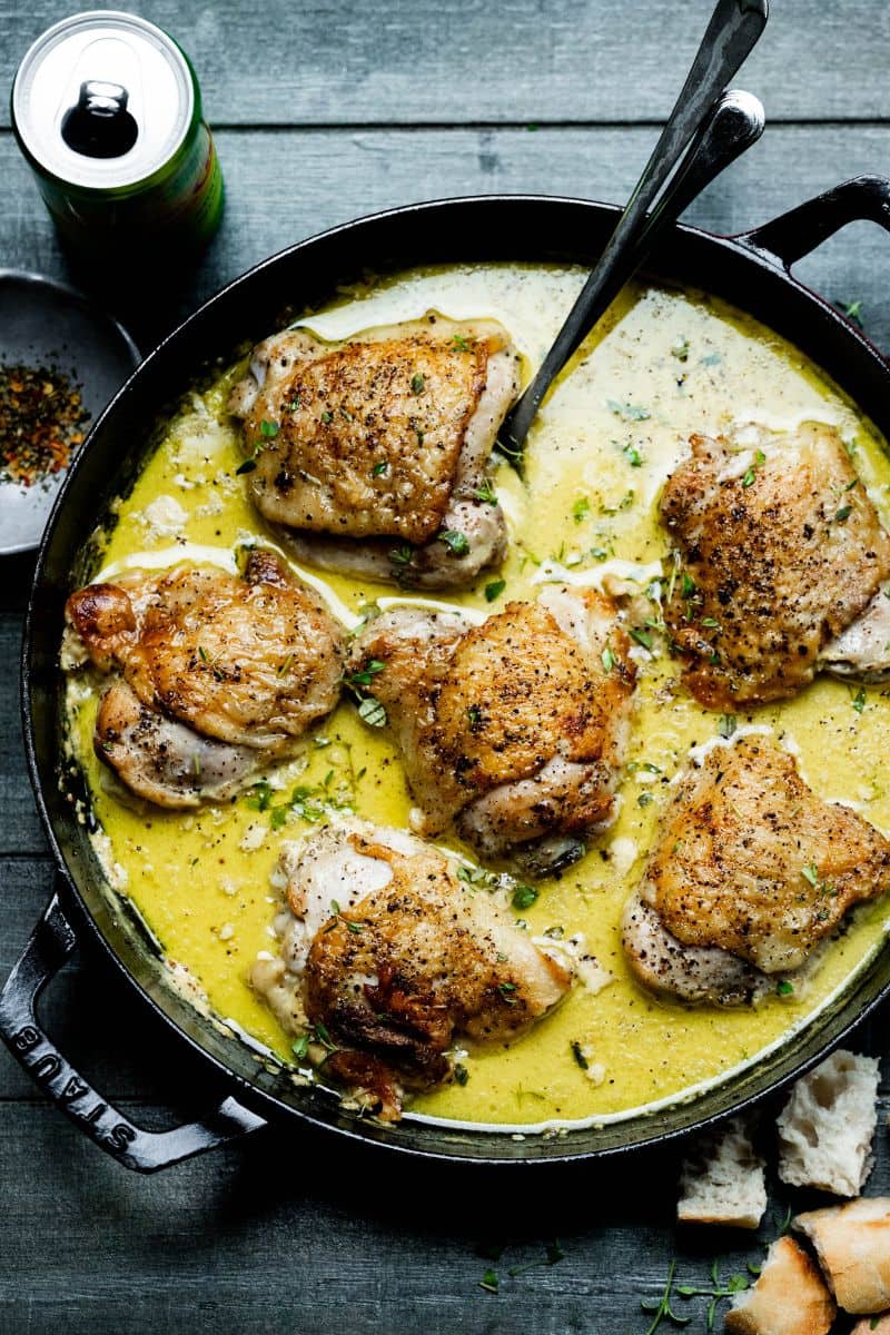 Six chicken thighs in a braiser with pan sauce and some herbs.