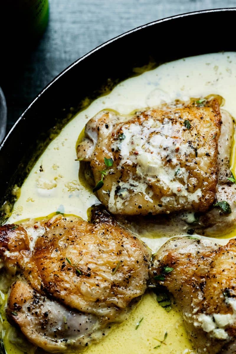 Close up of saucy chicken thighs with thyme sprigs.