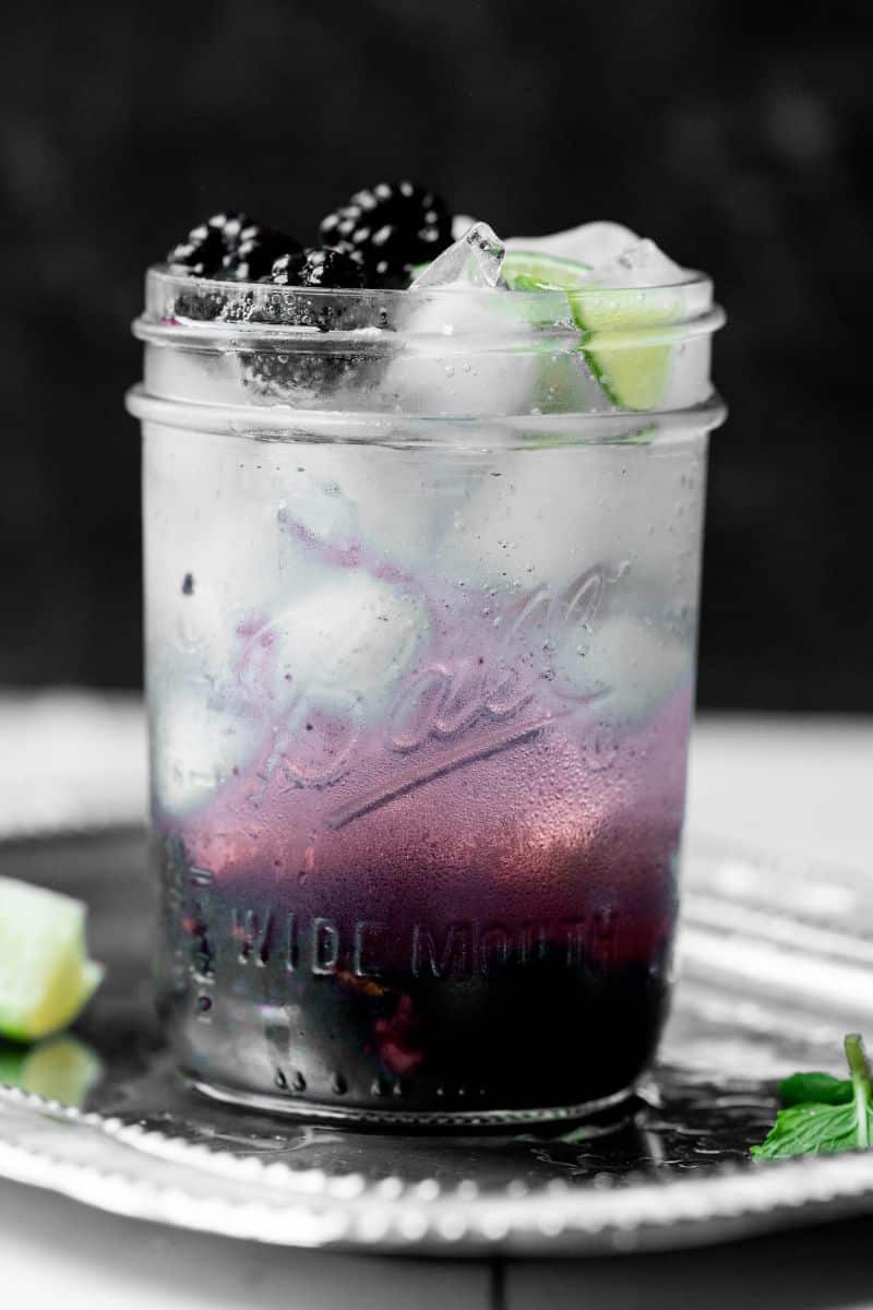 Front on image of blackberry mojito with lime garnish and bubbles.