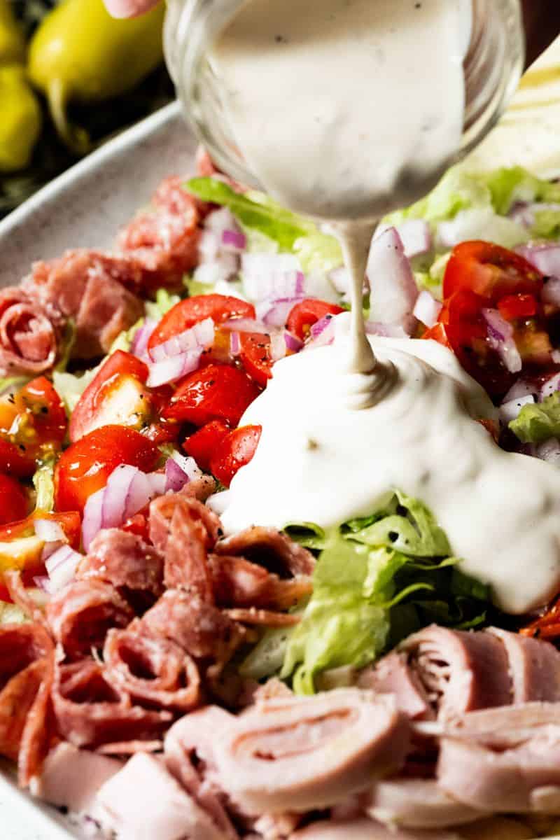 Salad dressing going onto a salad on a plate.