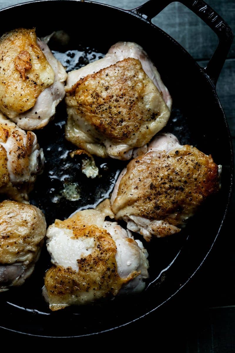 Pan seared chicken thighs in a black pan.